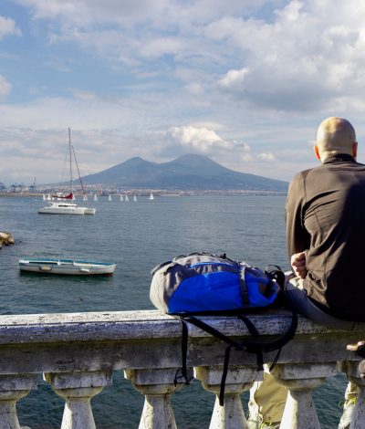 Tourist,Sitting,On,The,Wall,Observes,The,Panorama,Of,Vesuvius